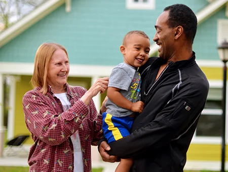 Smiling man holding a child while a woman tickles the child's back